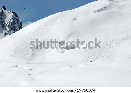 2 skiers below vast areas of powder snow on the mt blanc. High in the sky the tiny cabins which cross from france to italy
