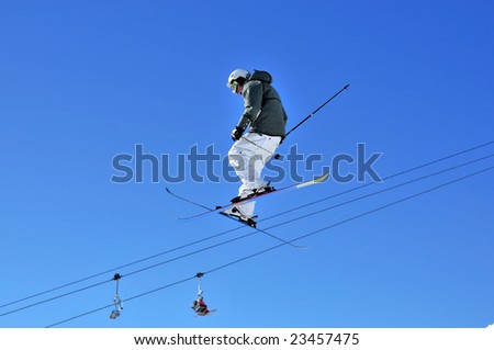 Aeroski: a male skier with white pants on a high jump with a relaxed posture, considering the risk