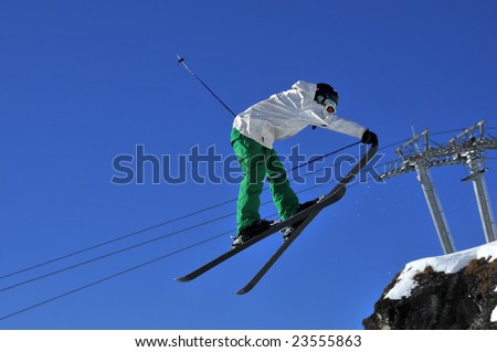 Aeroski: a skier in white jacket  touches the tip of the left ski with his right hand during a high jump