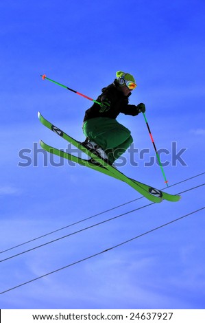 Skier with green skis, making a high jump with chair lift wires in the background