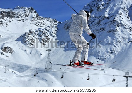 a skier in bright clothing performs a high jump with mountains and ski lifts in the background