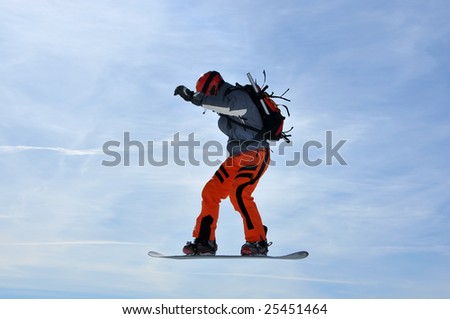 a snowboarder with avalanche kit performing a high jump against a blue sky