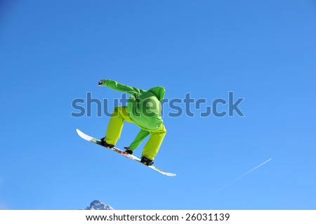 a snowboarder dressed in lime green performing a high jump trailing snow thrown up by the jump