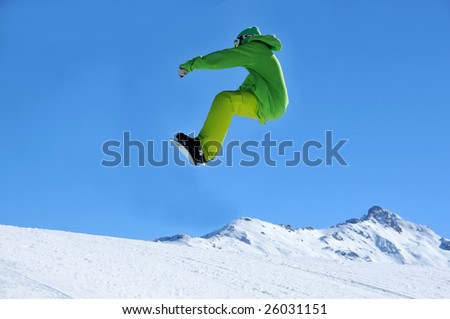 a snowboarder clothed in green coming in to land following a jump