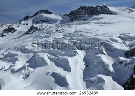 snow covered crevasses on a glacier. In the background ski lifts and ski runs at over 11000 feet altitude in the swiss alps