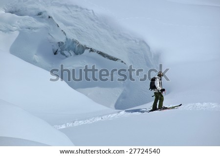 a skier on a glacier passes over a snow bridge on a crevasse, just behind him, the blue ice of the bare glacier is clearly visible.
