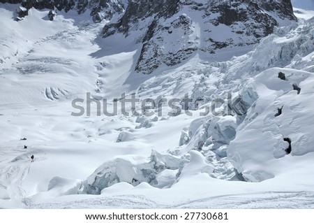 a large ice fall on a glacier with mountains in the background. Fresh snow covers the glacier, and clear blue ice can be seen on exposed blocks in the ice fall