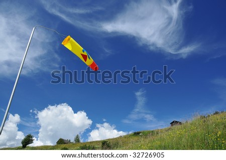 a windsock used for para-glider take-offs is blow horizontally. In the background alpine chalets in flower filled meadows