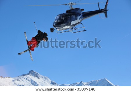 a helicopter equipped with a steady cam films a skier performing a jump with crossed skis.