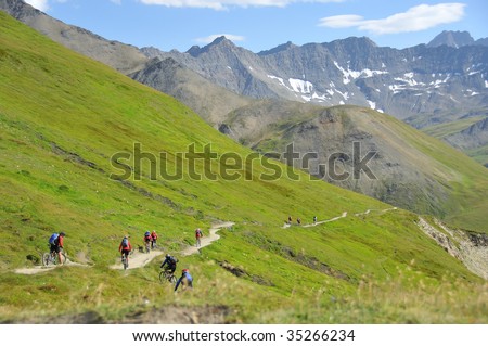 a group of mountain bikers on the tour around mont blanc descending from switzerland into italy on a narrow path