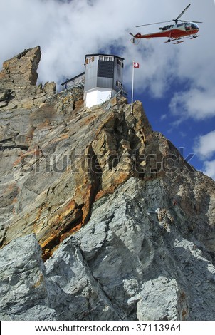 mountain refuge clinging to a rocky spike above glaciers can only be accessed by steep ladders from the glacier. The swiss flag flies in front of the building