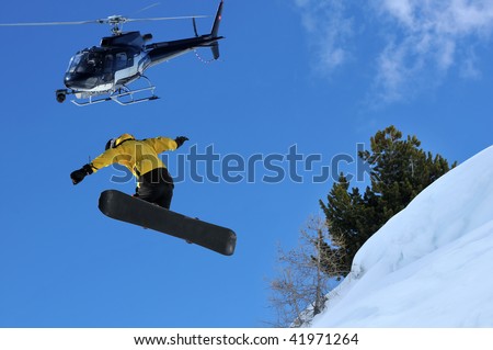 snowboarder jumping off a ridge of snow being filmed from a helicopter