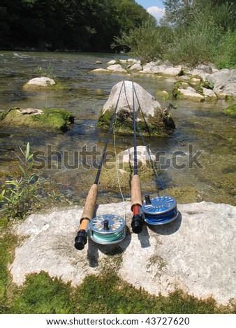 two fly fishing rods resting on stones on a clear trout river. One with floating, one with sinking line