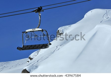 a six person chair lift with ski tracks in powder snow behind