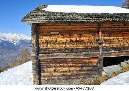 an old mountain log cabin in the snow the wood coloured by strong ultra violet sunlight