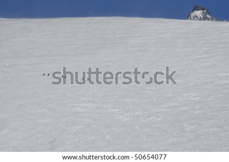 ski mountaineers cross a wide flat glacial expanse of ice. Strong winds cause drifting snow