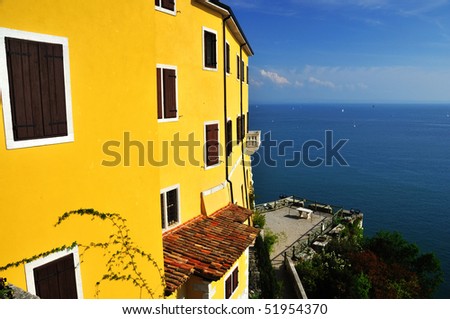An italian villa with yellow walls overlooks the mediterranean on a beautiful day. Yachts sail in the bay