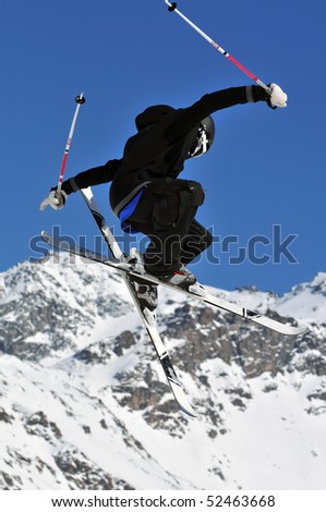 an elegantly dressed freestyle  ski jumper in black and white clothes against a back drop of mountains.