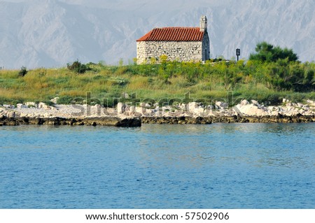 very old stone chapel stands alone on a small island in the sea with high mountains in the background