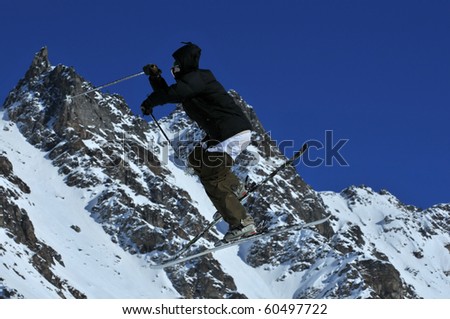 a ski jumper with black jacket, hood and underpants on the outside, snow covered mountains in the background