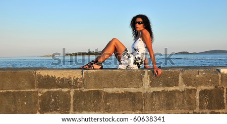 a latin girl with white summer cotton dress on a harbour wall on holiday