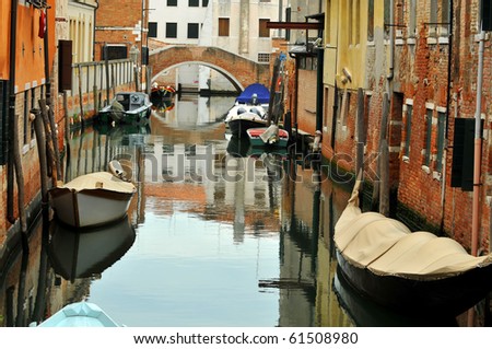 a typical canal in Venice with boats including a gondola tied up next to houses and a bridge over the waterway