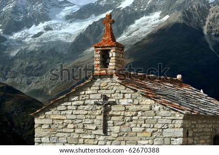 an old stone chapel with red lichen on the cross. In the background brooding glacier covered mountains