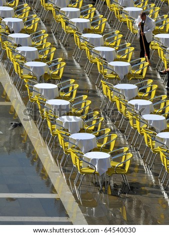 yellow chairs sit in water in a venice cafe as Venice slowly sinks into the sea, a waiter brushes the water away