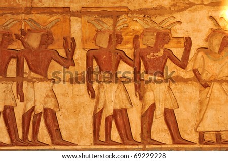 Ancient Egyptian bas-relief of a procession of porters carrying steps to the royal throne with ceremonial feathers in their caps