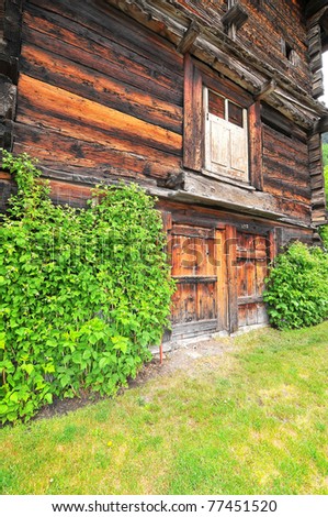 Charming wooden cabin with two entrance doors, indicating that it is shared between two owners, with mowed grass outside, and raspberry canes