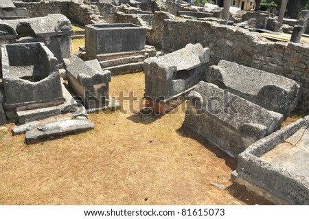 cemetery in a roman town, with large stone sarcophagi lying around, all of which have been broken open and robbed