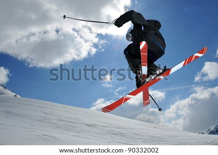 A free-ride ski jumper, with skis crossed against a blue sky with clouds