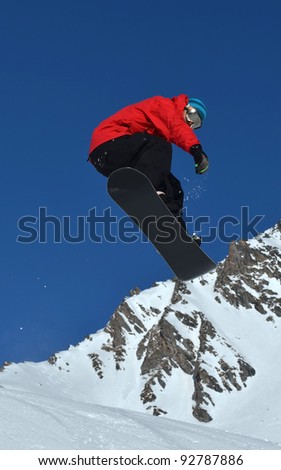 A free rider in red and black on a snowboard performing a high jump. Against a background of high mountains