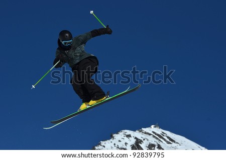 Free rider dressed in black with helmet makes a jump and turn high in the air against a clear blue sky.