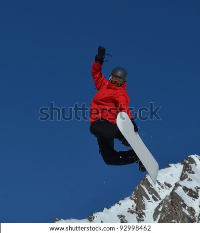 Snowboarding Free Rider in red and black performing a board grab, and trailing snow against a clear blue sky