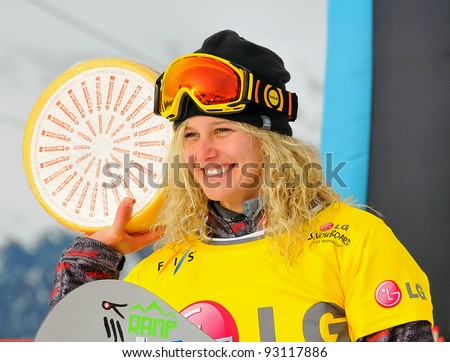 VEYSONNAZ, SWITZERLAND - JANUARY 19: Lindsay Jacobellis (USA) holds up Swiss cheese while at the podium after winning the 2012 world championship at the FIS World Cup Snowboard Cross finals on January 19, 2012 in Veysonnaz, Switzerland