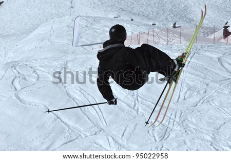 a free ride ski jumper clothed all in black, performing a jump and a grab, against a background of tracks in the snow