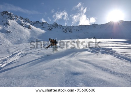 Off trail snowboarder in deep powder snow makes a turn spraying powder in his wake in bright sunshine