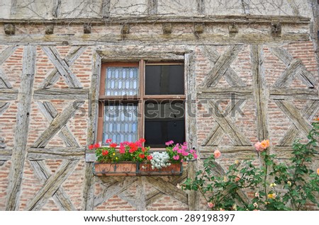 A traditional half timbered house with simple saltires and brick filling , decorated with climbing roses and geraniums