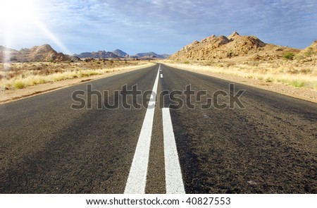 A straight road with sun and mountains