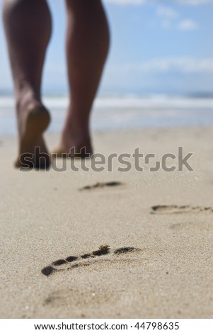 The well formed calves of a  person walking on the beach leaving behind only footprints