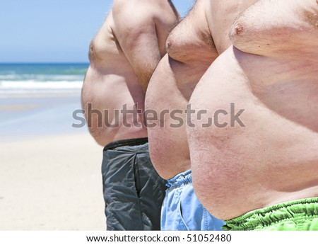 Close up of three obese fat men on the beach showing their unhealthy bellies