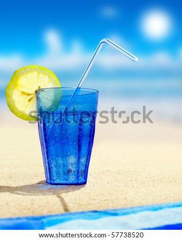 Close up of a blue glass with sparkling water and lemon on a beach