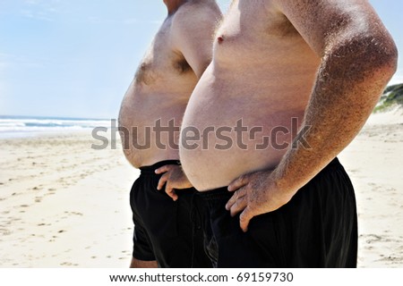 Close up of two fat men showing their bellies on the beach