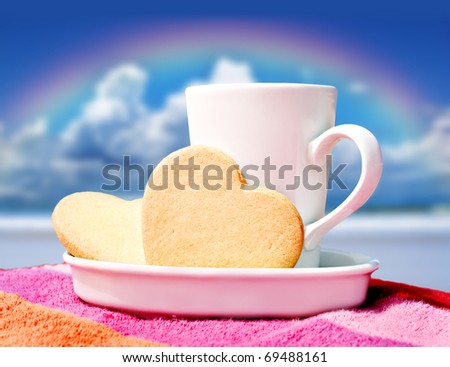Mug of coffee and heart shaped cookies on a tropical beach with a rainbow in the background