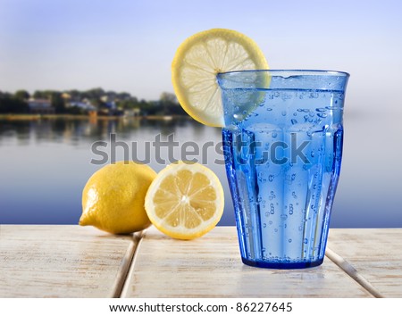 a Blue glass with sparkling water and lemon on a wooden deck overlooking the calm water of a tropical lagune