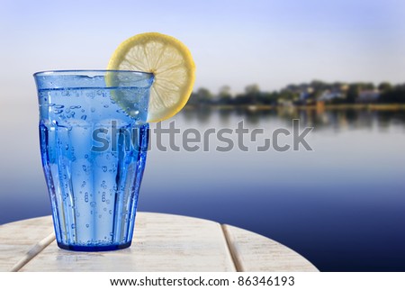 a Blue glass with sparkling water and lemon on a wooden deck overlooking the calm water of a tropical lagune