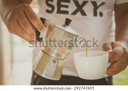 A man pouring coffee from moka pot to a cup of coffee.