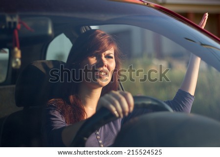 Closeup portrait, angry young sitting woman pissed off by drivers in front of her and gesturing with hands. Road rage traffic jam concept