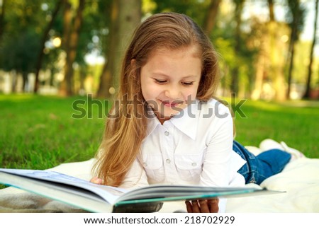 pretty little girl reading book in park